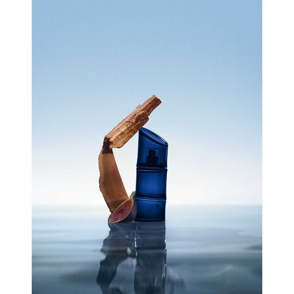 Blaues Parfümflakon mit Holz und Frucht auf Wasser. Reflektion sichtbar. Blauer Hintergrund.