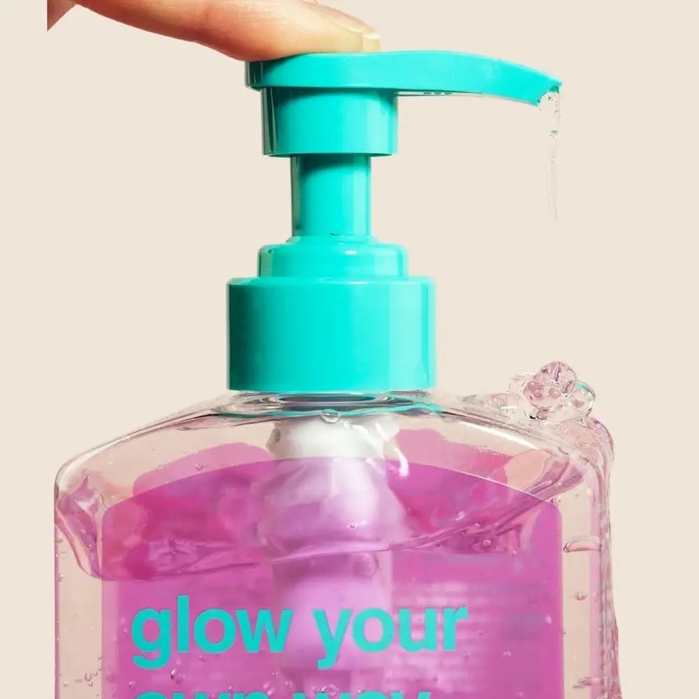 Nahaufnahme einer transparenten Flasche mit türkisfarbenem Pumpkopf. Flüssigkeit wird aus dem Spender gedrückt.