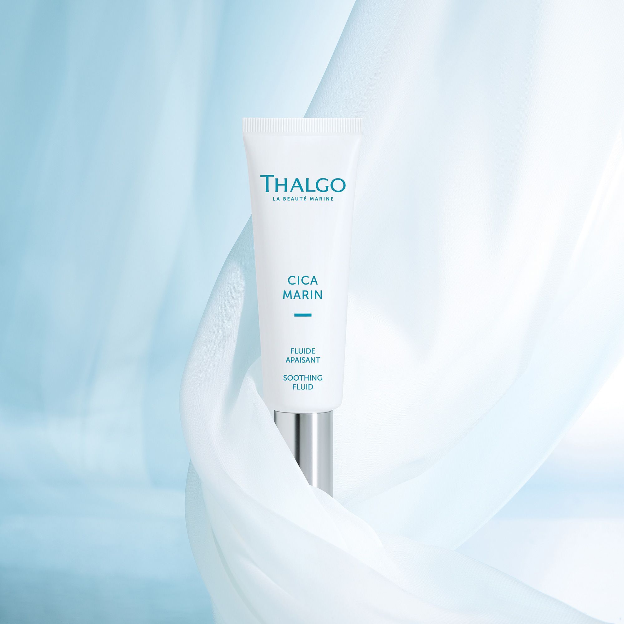 Weiße Tube mit silbernem Verschluss, vor blauem Hintergrund mit Stoff. Aufschrift: THALGO, CICA MARIN, Fluide Apaisant, Soothing Fluid.