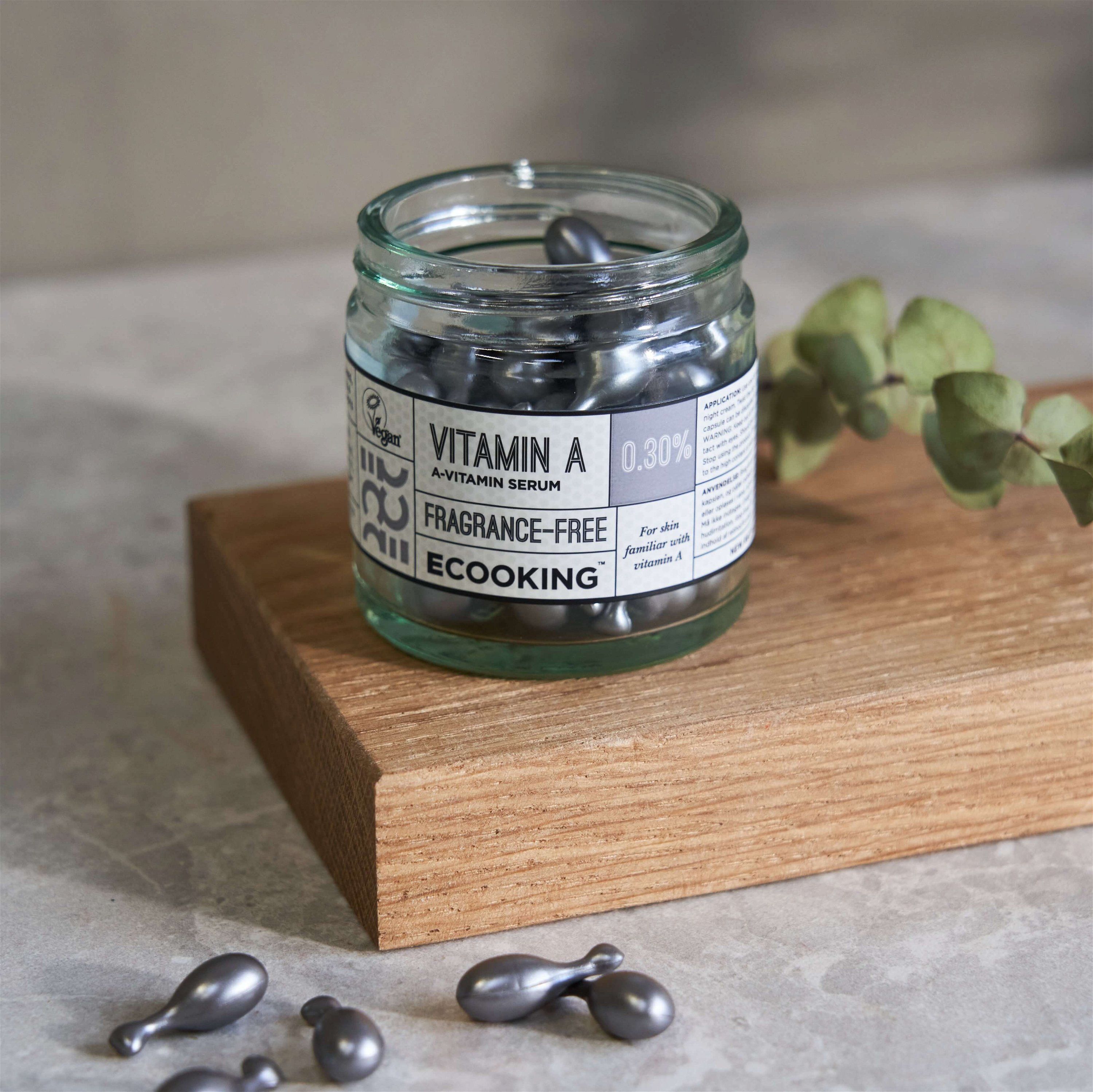 Glas mit Kapseln auf Holzbrett. Aufschrift: Vitamin A 0,30%, Fragrance-Free, Ecooking. Vegan-Siegel.