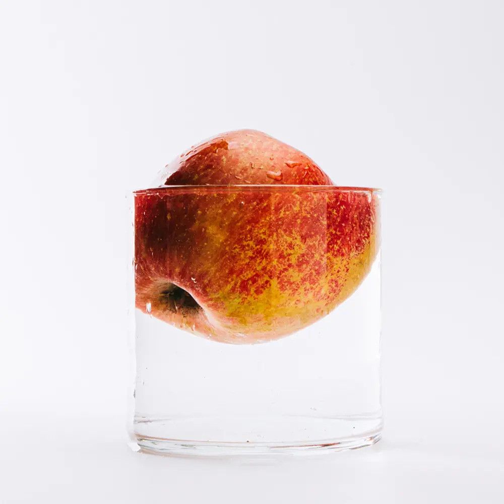 Apfel in einem Glas Wasser. Der Apfel ist teilweise untergetaucht. Rote und gelbe Farbe.