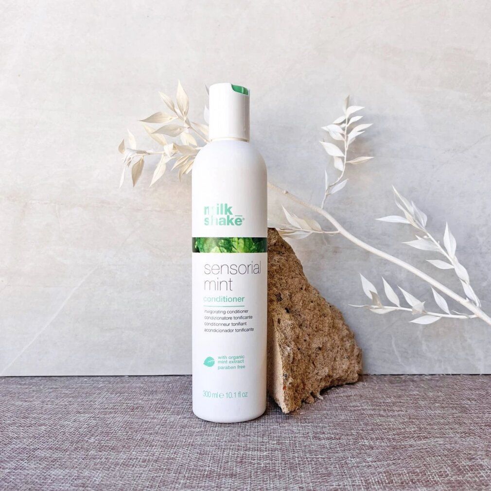Weiße Flasche mit grünem Aufdruck. Beschriftung: milk_shake, sensorial mint conditioner. Enthält Minzextrakt. Volumen: 300 ml. Auf Stein und Dekoration.