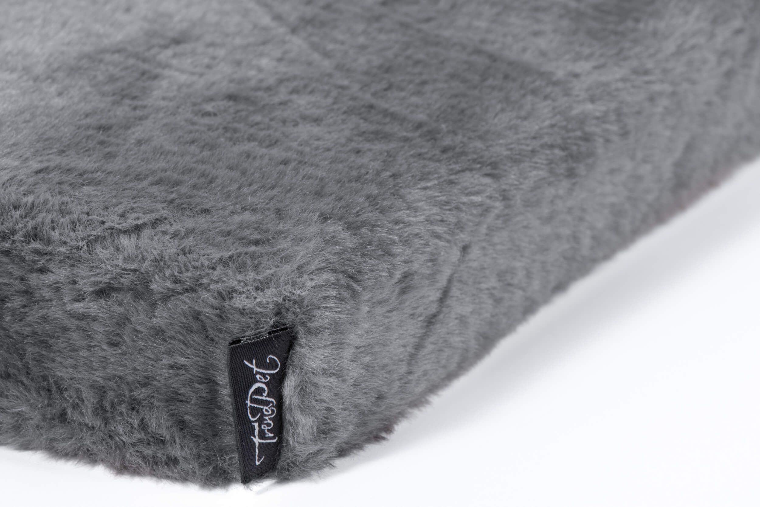 Graue, rechteckige Hundematratze mit Fellstruktur. Schwarzes Etikett mit TrendPet-Logo.