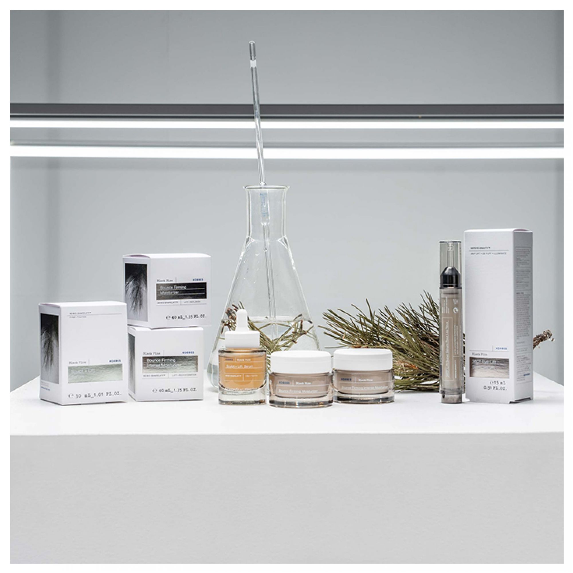 Mehrere Korres Black Pine Produkte, darunter Seren und Cremes, arrangiert mit Laborutensilien.