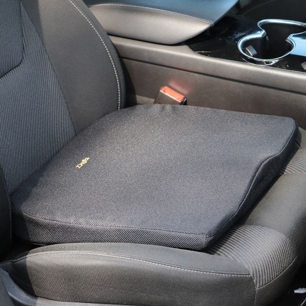 Schwarzes Keilkissen auf einem Autositz. Goldfarbenes Logo sichtbar. Quadratische Form mit abgerundeten Ecken.