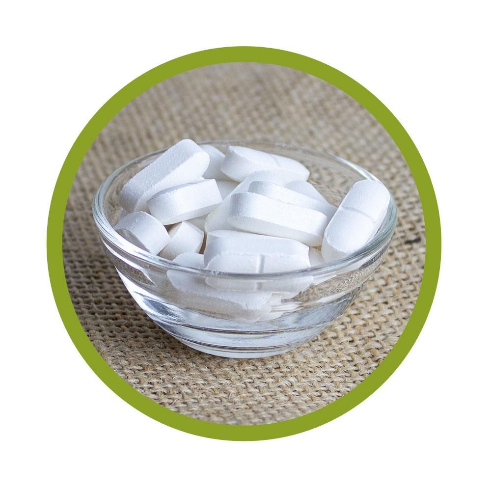 Klare Glasschale mit weißen Tabletten. Auf grobem Untergrund platziert. Grüne Umrandung.