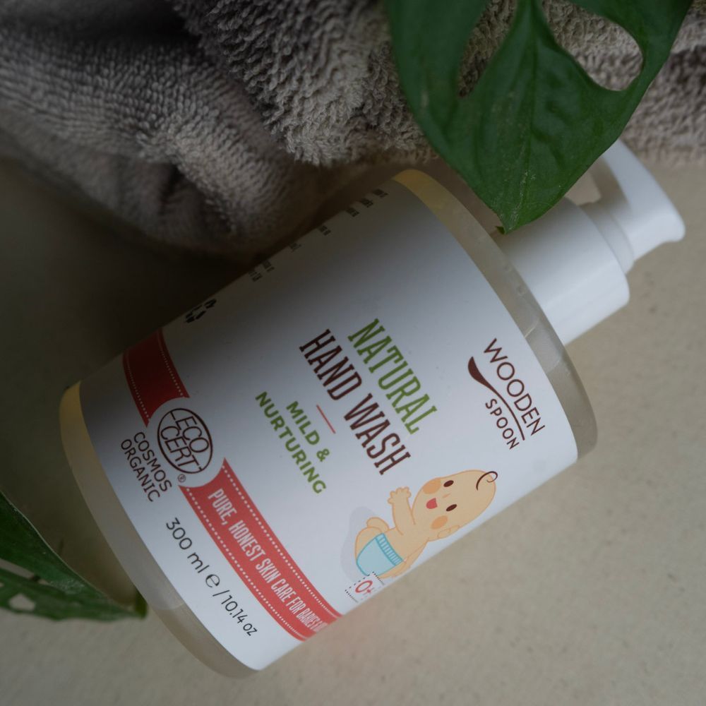 Flüssigseife-Flasche mit Pumpe, liegend. Etikett mit "NATURAL HAND WASH", Baby-Illustration und "COSMOS ORGANIC"-Zertifizierung. 300 ml.