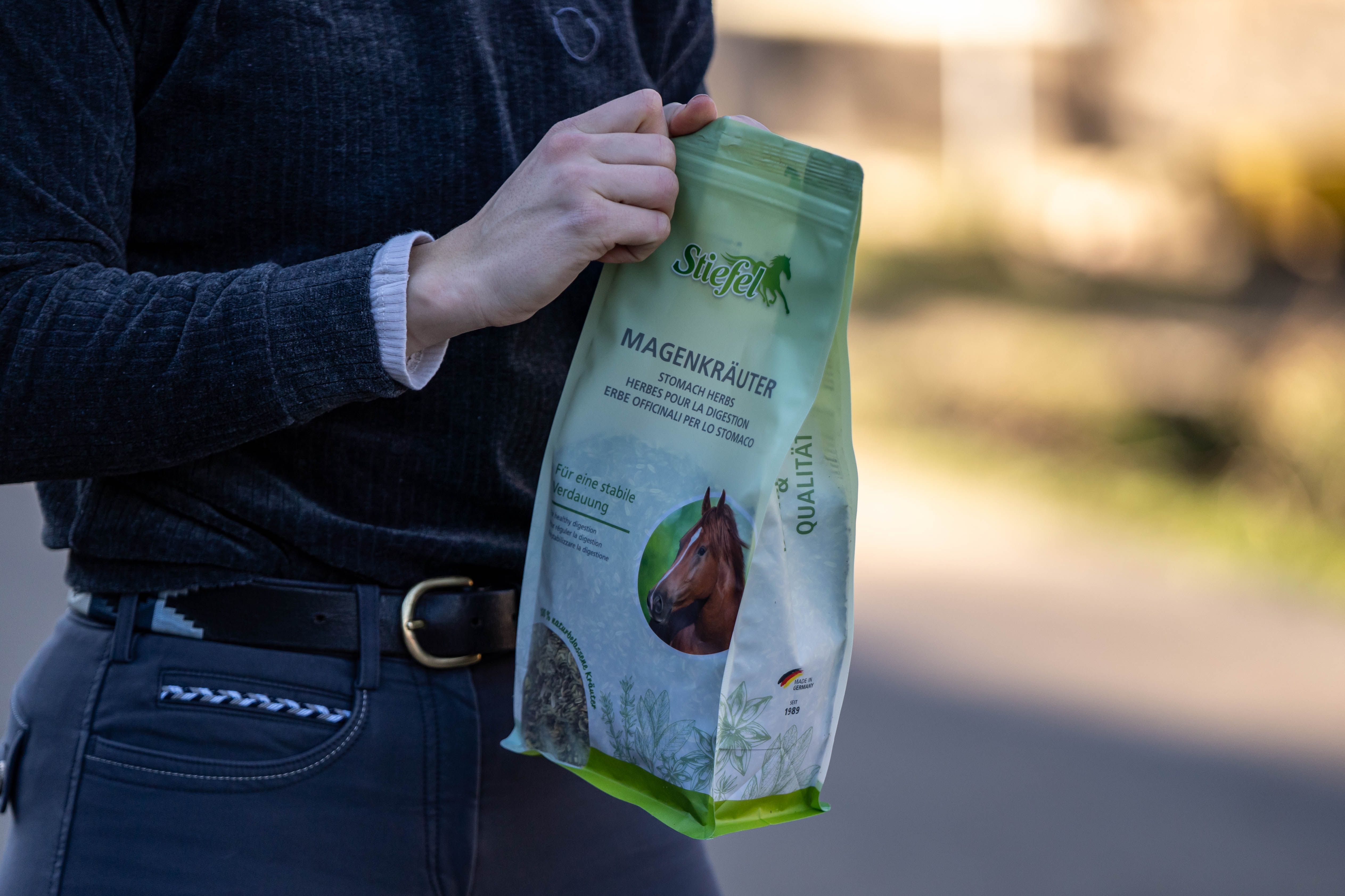 Person hält eine grüne Tüte Stiefel Magenkräuter. Produktverpackung mit Logo und Produktbezeichnung.