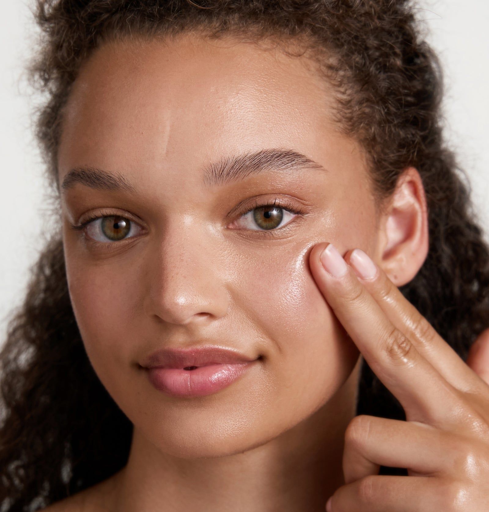 Frau berührt Gesicht. Haut glänzt. Helle Haut. Finger berühren die Wange. Natürliches Licht.