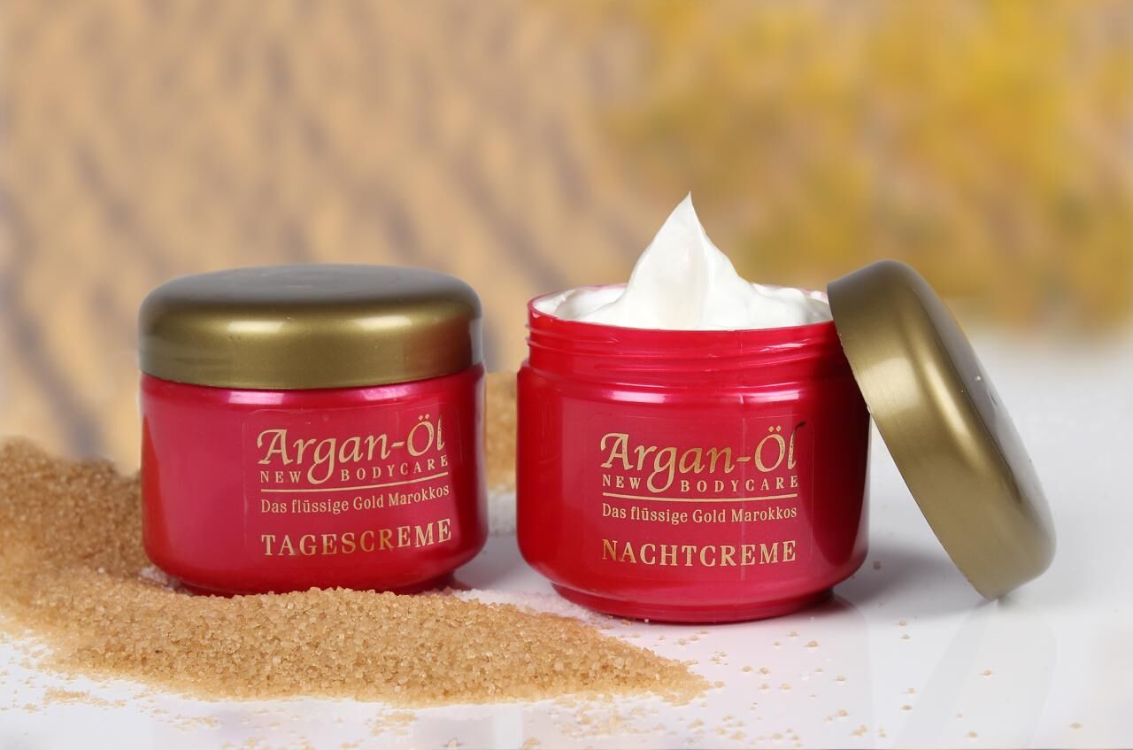 Zwei rote Tiegel mit goldenen Deckeln. Aufschrift: Argan-Öl, Nachtcreme und Tagescreme. Ein Tiegel geöffnet mit Creme.