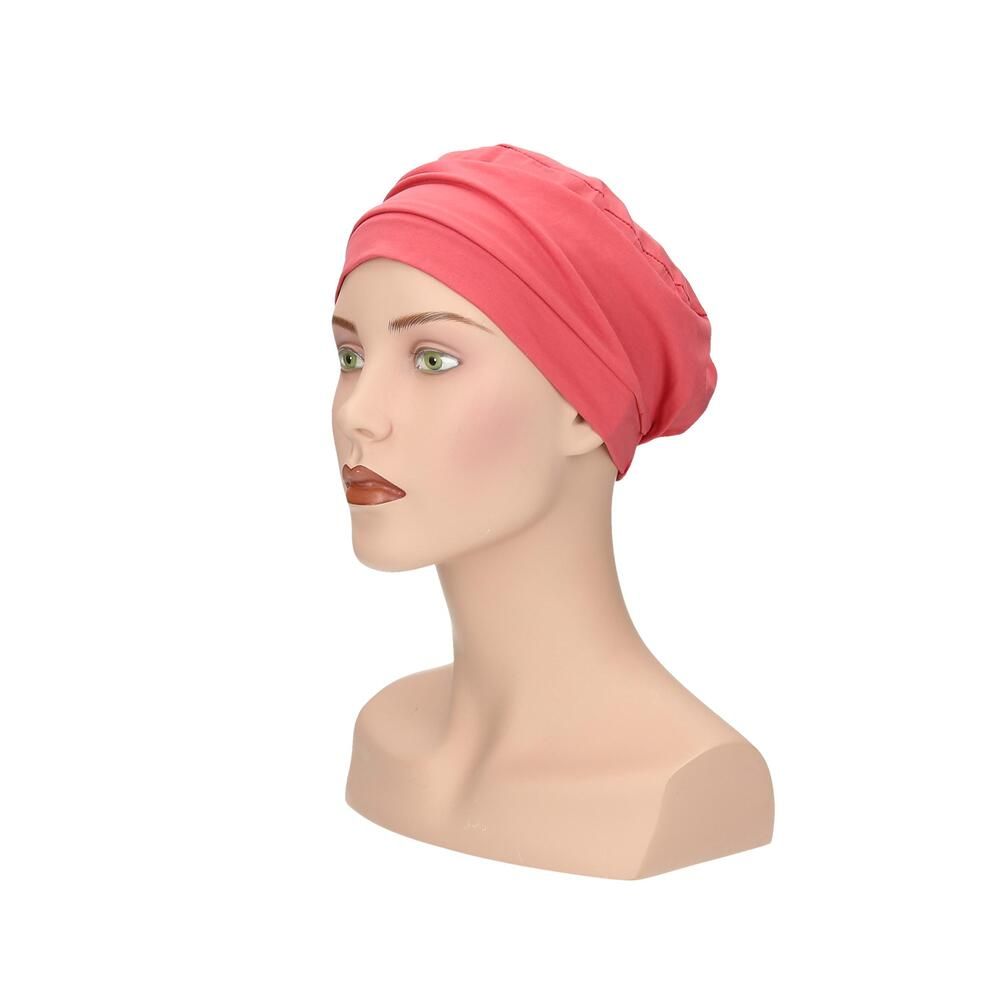 Korallenfarbener Turban auf Büste. Stoffhaube mit Faltenwurf. Seitenansicht.