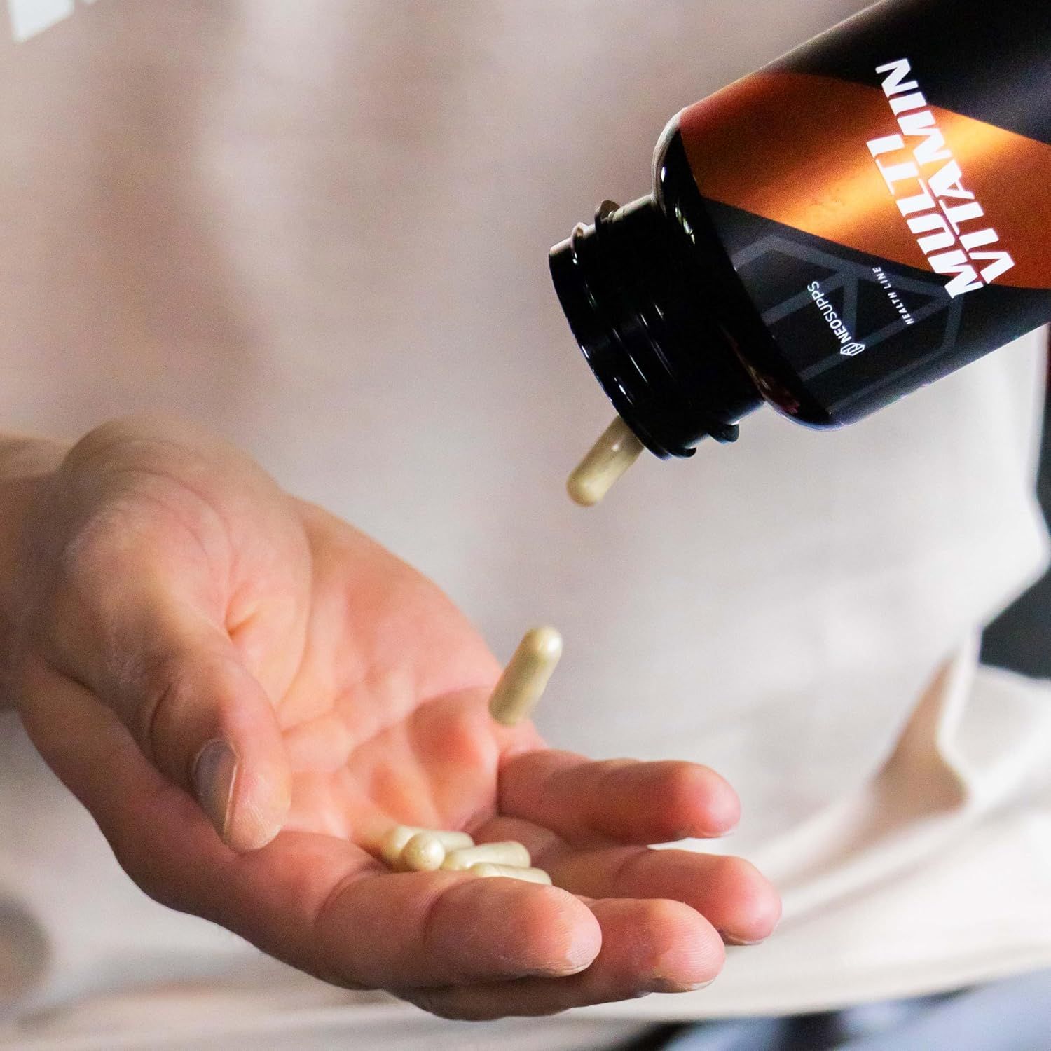 Person schüttet Kapseln aus einer Flasche in die Hand. Schwarze Flasche mit "Multi Vitamin"-Etikett.