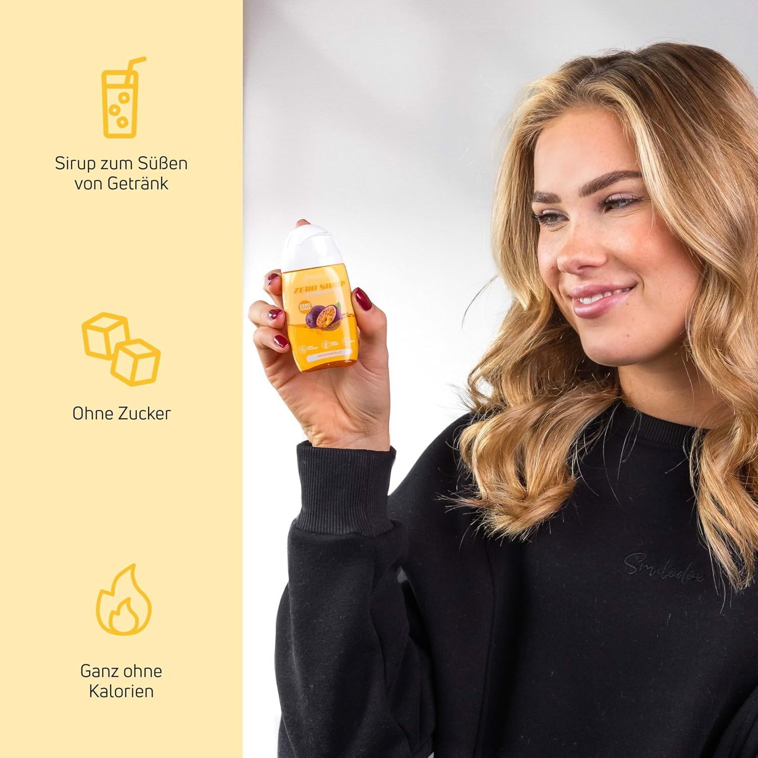 Frau hält eine Flasche Sirup. Auf der Flasche steht: Ohne Zucker, Ganz ohne Kalorien. Gelbe Flasche mit gelbem Etikett und Passionsfrucht.