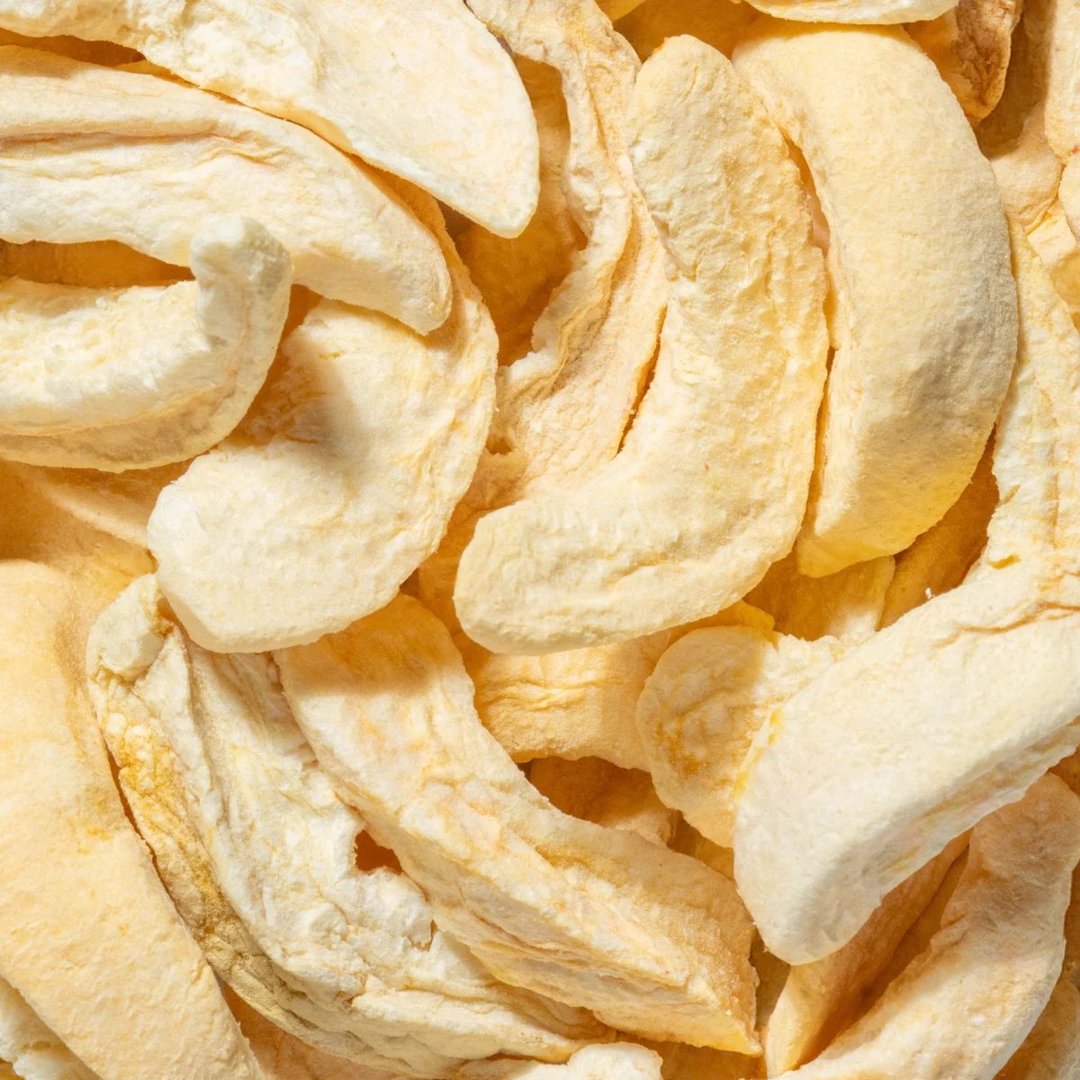 Nahaufnahme von gefriergetrockneten Pfirsich-Scheiben. Helle, beige Farbe. Einzelne Stücke mit unregelmäßiger Form.