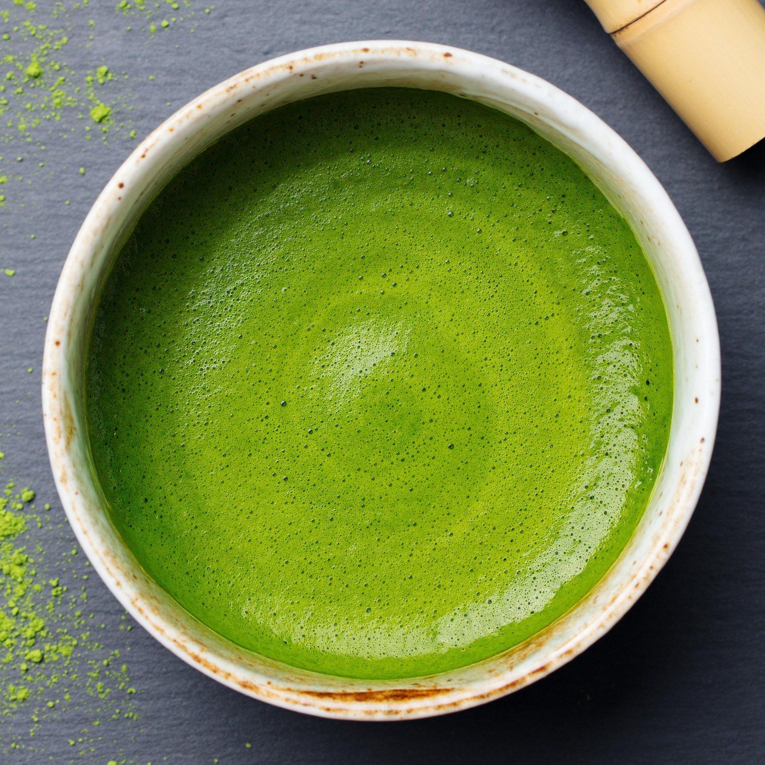 Eine Schüssel mit geschlagenem Matcha-Tee. Der Tee ist hellgrün und schaumig. Ein Bambusbesen liegt daneben.