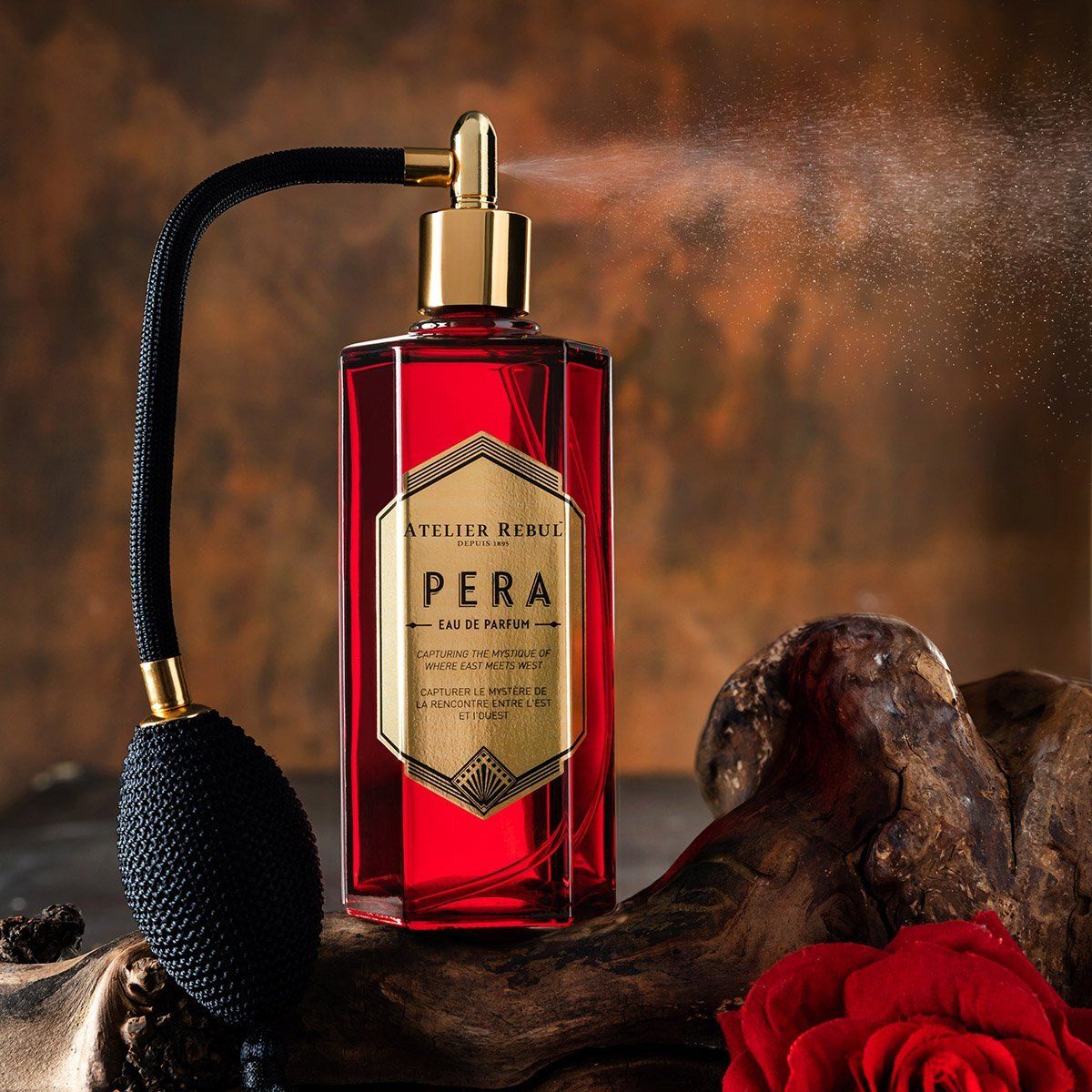 Rotes Parfumflakon mit schwarzem Zerstäuber. Goldene Details und Etikett mit Text. Sprühnebel. Atelier Rebul Pera Eau de Parfum.