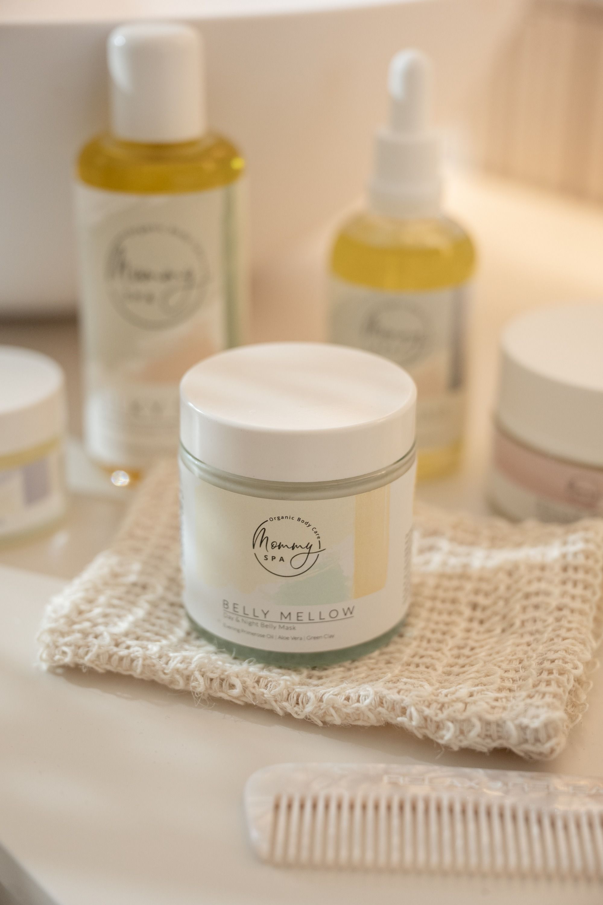 Mommy SPA Belly Mellow Creme-Maske auf einer Waschlappen. Weitere Produkte im Hintergrund. Weißer Behälter mit Logo.