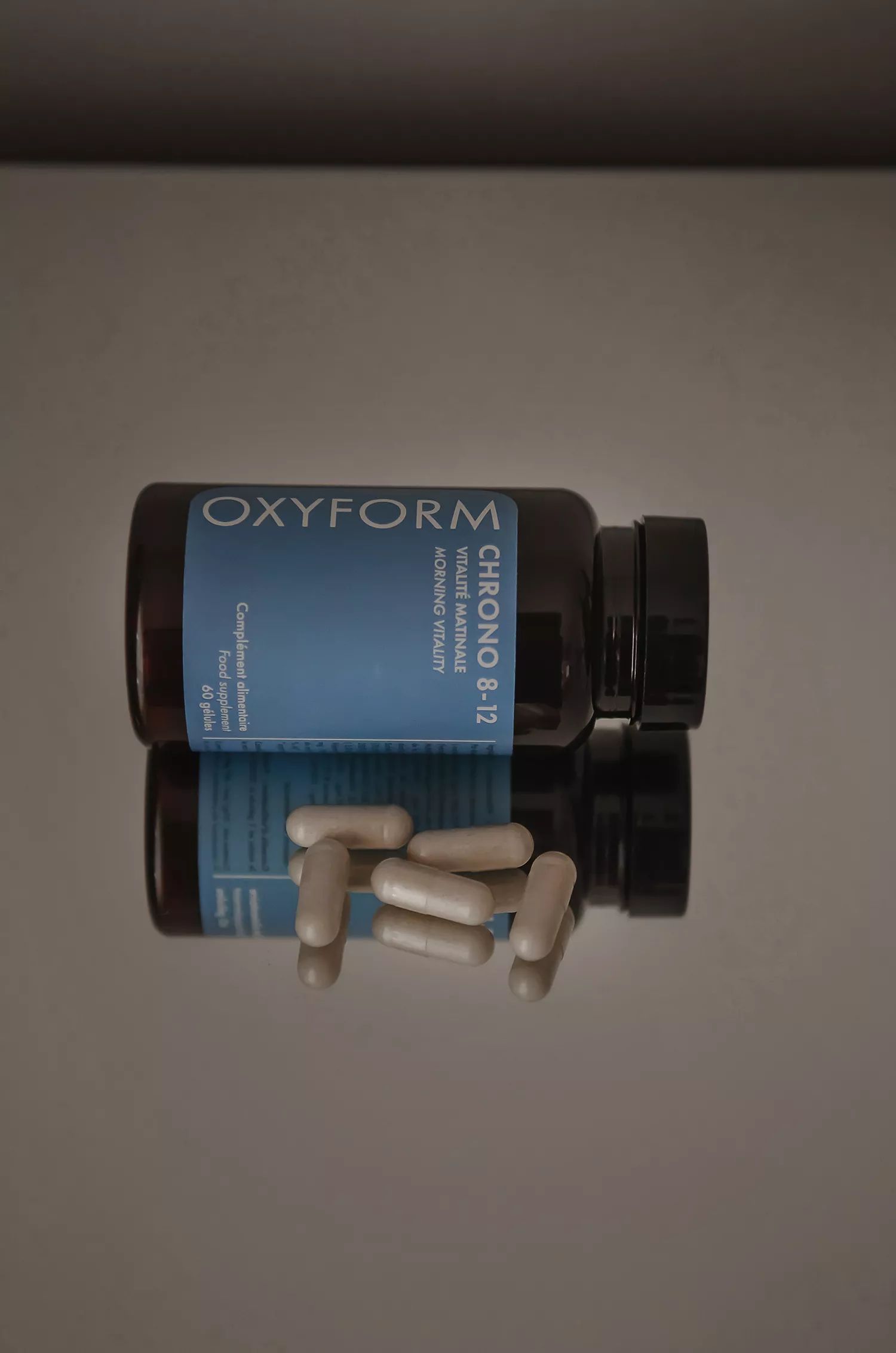 Braune Flasche mit blauer Aufschrift. Einige Kapseln liegen daneben. Produktname: Oxyform Chrono 8-12.