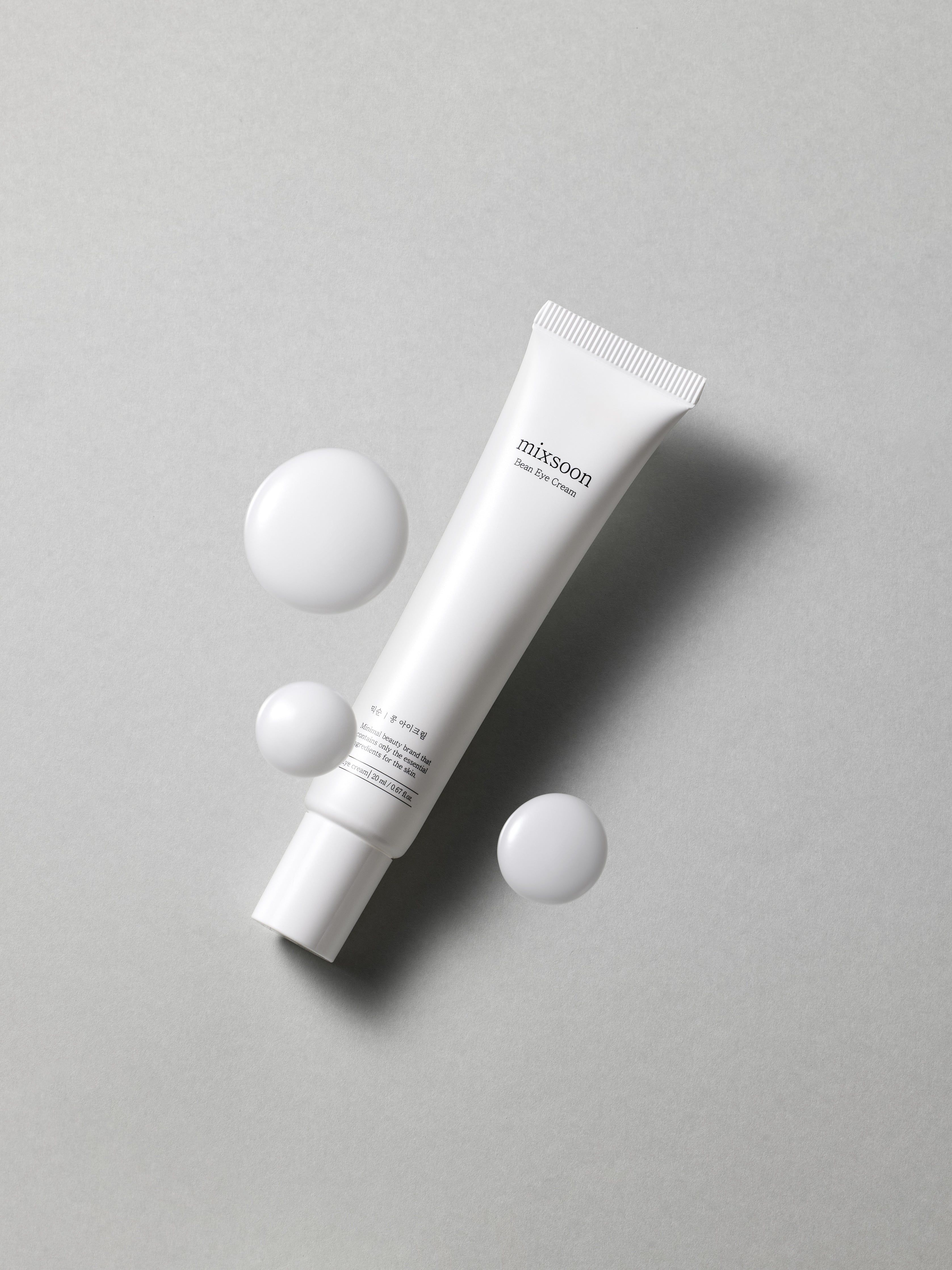 Weiße Tube "mixsoon Bean Eye Cream" mit weißen Tropfen. Aufschrift auf der Tube. Grauer Hintergrund.