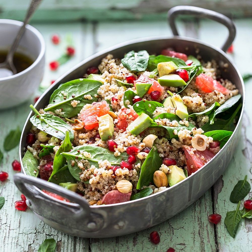 Salat in Metallschale. Zutaten: Quinoa, Spinat, Avocado, Granatapfelkerne, Nüsse. Auf Holzuntergrund.