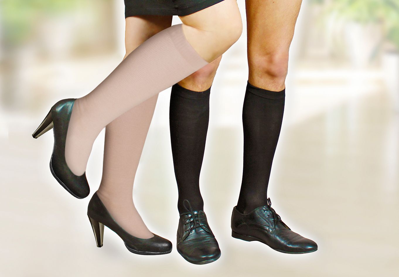 Zwei Personen mit Kompressionsstrümpfen. Eine Person trägt beige Strümpfe mit Pumps, die andere schwarze Strümpfe mit Schuhen.