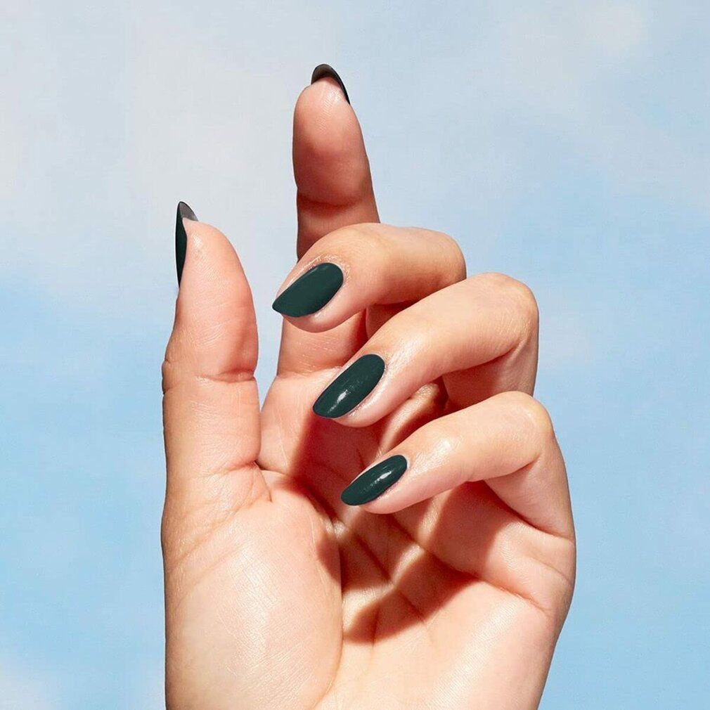 Hand mit lackierten, oval geformten Nägeln in Grün. Blauer Himmel im Hintergrund.