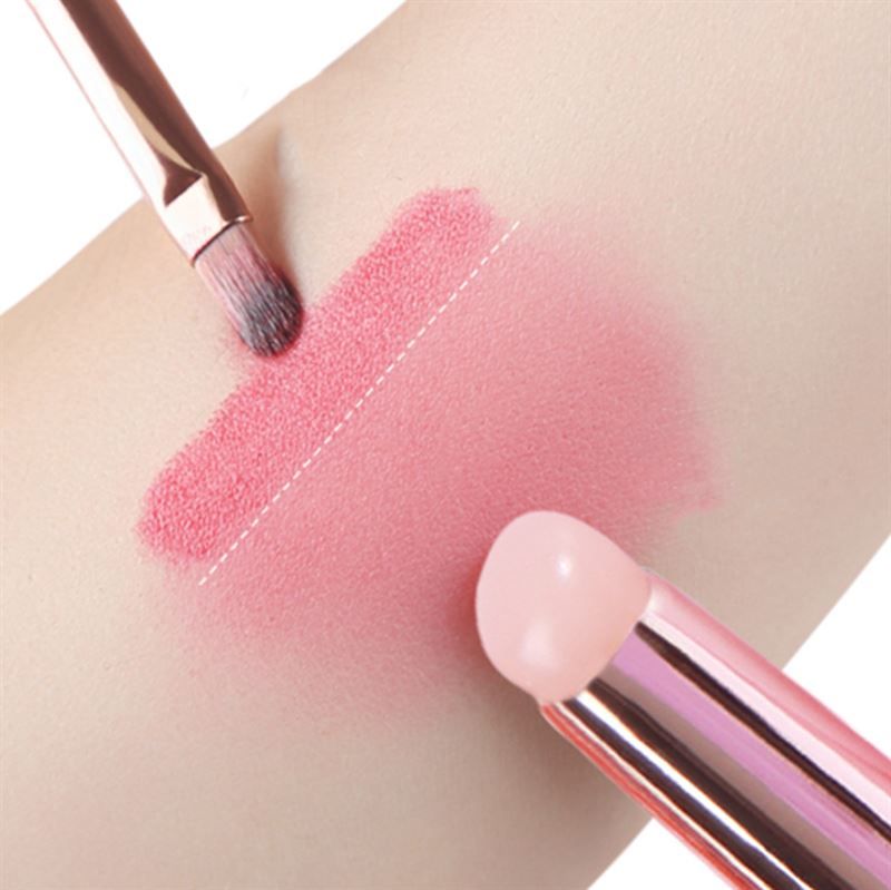 Zwei Pinsel auf Haut. Ein Pinsel trägt rosa Produkt auf. Der andere Pinsel ist in der Nähe.