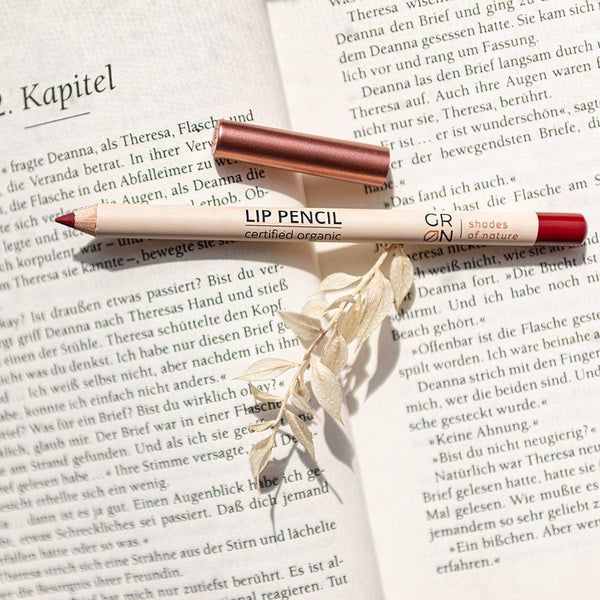 Lippenstiftstift mit kupferfarbener Kappe auf einem Buch. Aufschrift: LIP PENCIL, GRN, certified organic.