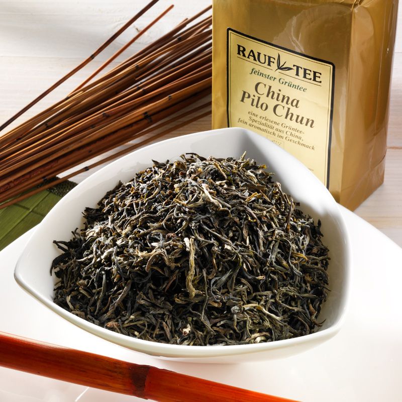 Schale mit losem grünem Tee. Rauf Tee China Pi Lo Chun-Packung im Hintergrund.
