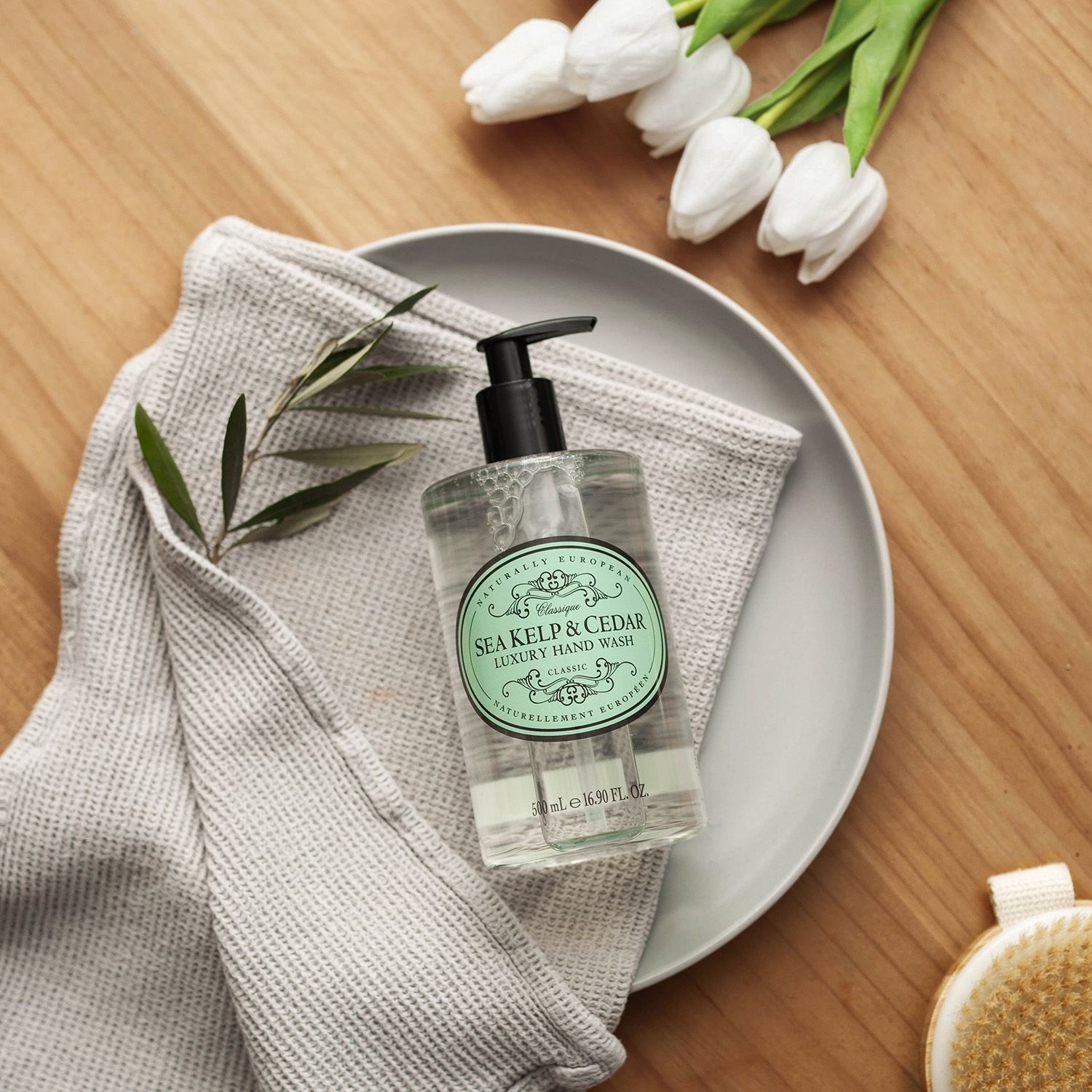 Flüssigseife mit Pumpspender auf Teller und Handtuch. Aufschrift: Sea Kelp & Cedar Luxury Hand Wash.