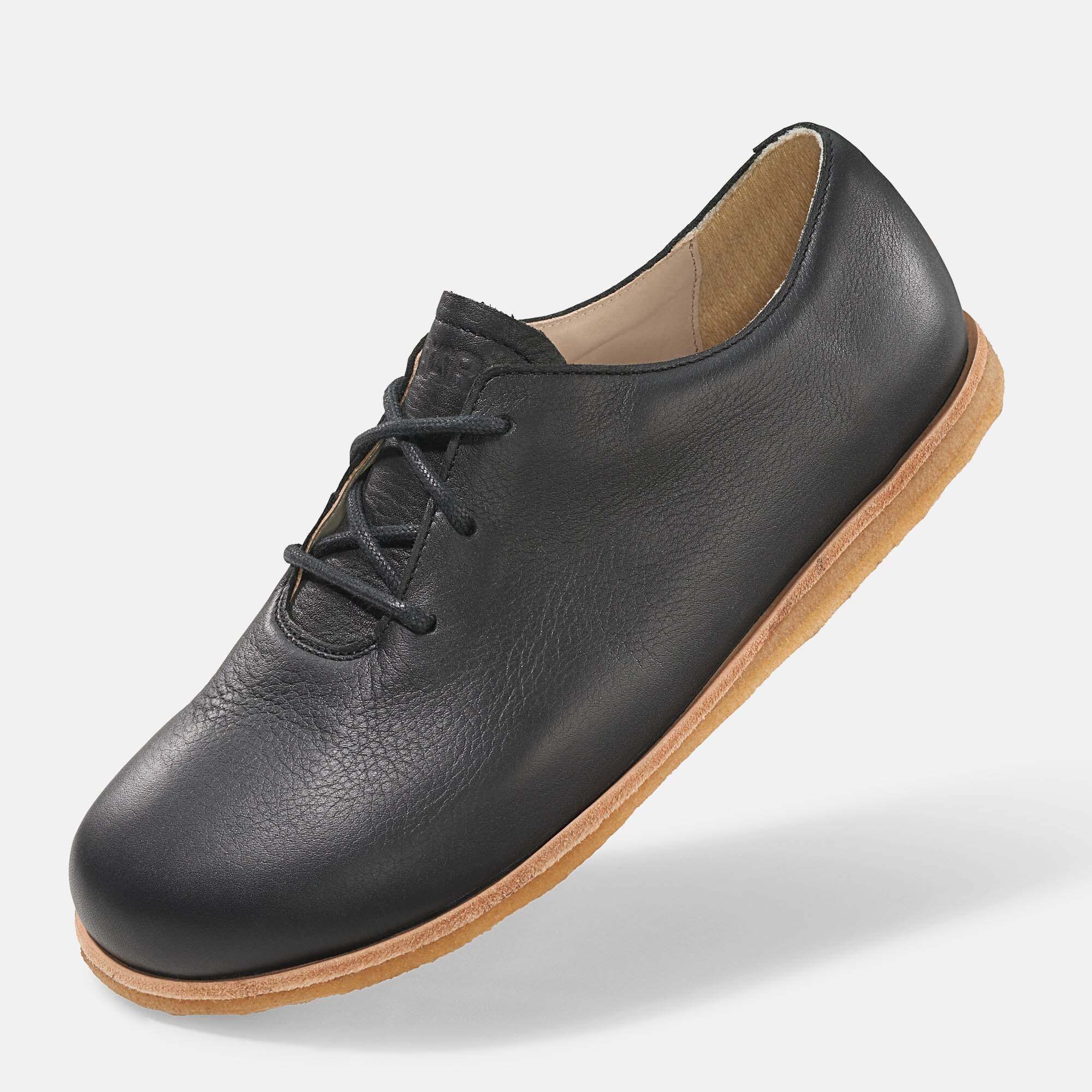 Schwarzer Lederschnürschuh mit heller Sohle. Schuh leicht schräg gestellt.