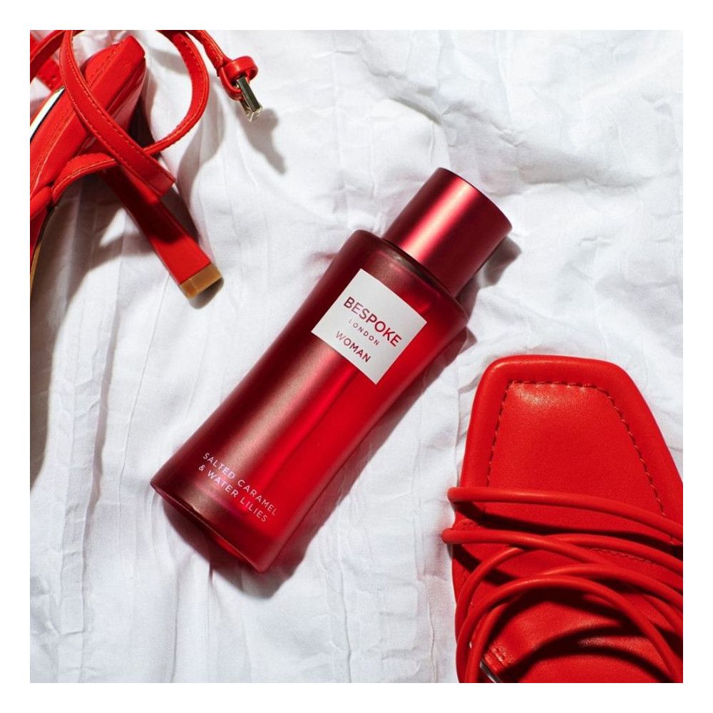 Rote Flasche auf weißem Stoff, umgeben von roten Schuhen. Aufschrift: Bespoke London Woman. Text: Salted Caramel & Water Lilies.