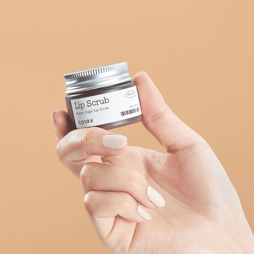Eine Hand hält einen kleinen Tiegel mit "Lip Scrub Honey Sugar Lip Scrub COSRX".