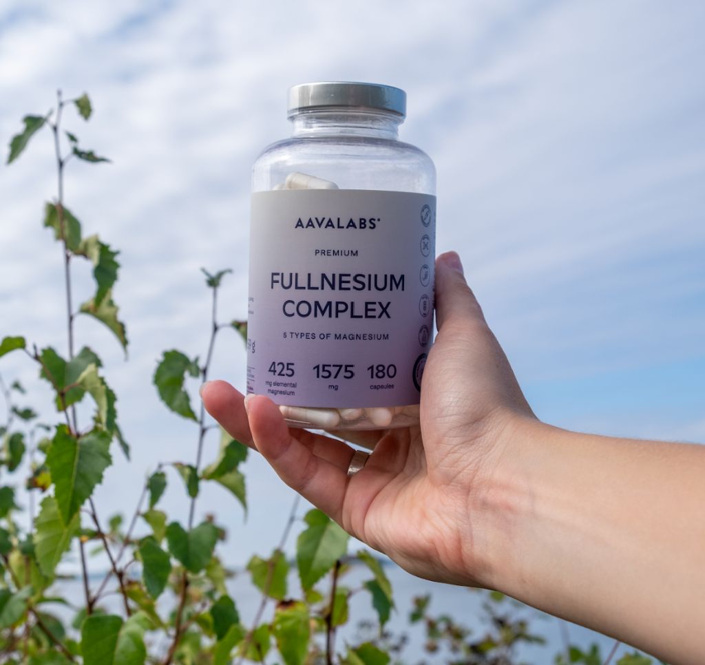 Hand hält eine Flasche Fullnesium Komplex. Hintergrund: Natur, blauer Himmel. 180 Kapseln.