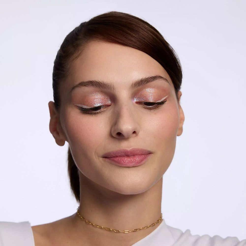 Eine Frau mit weißem Eyeliner und glänzendem Lidschatten. Sie trägt eine goldene Halskette.