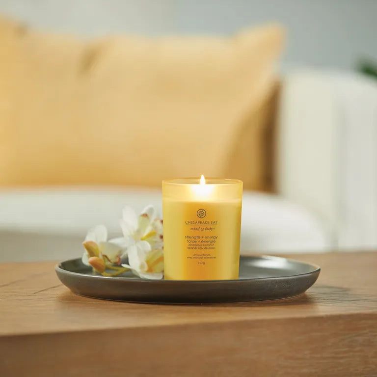 Brennende gelbe Kerze auf einem Tablett mit Blumen. Text: Chesapeake Bay, mind & body, strength + energy, 250 g.