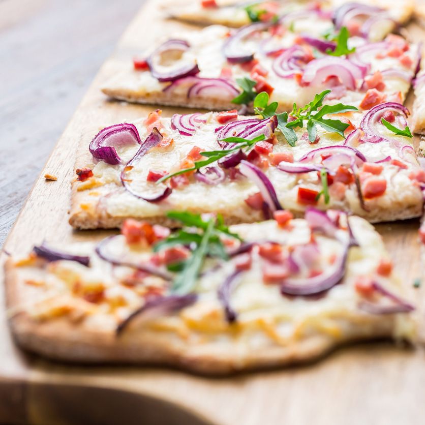 Flammkuchenstücke mit Zwiebeln, Speck und Rucola auf Holzbrett. Nahaufnahme.