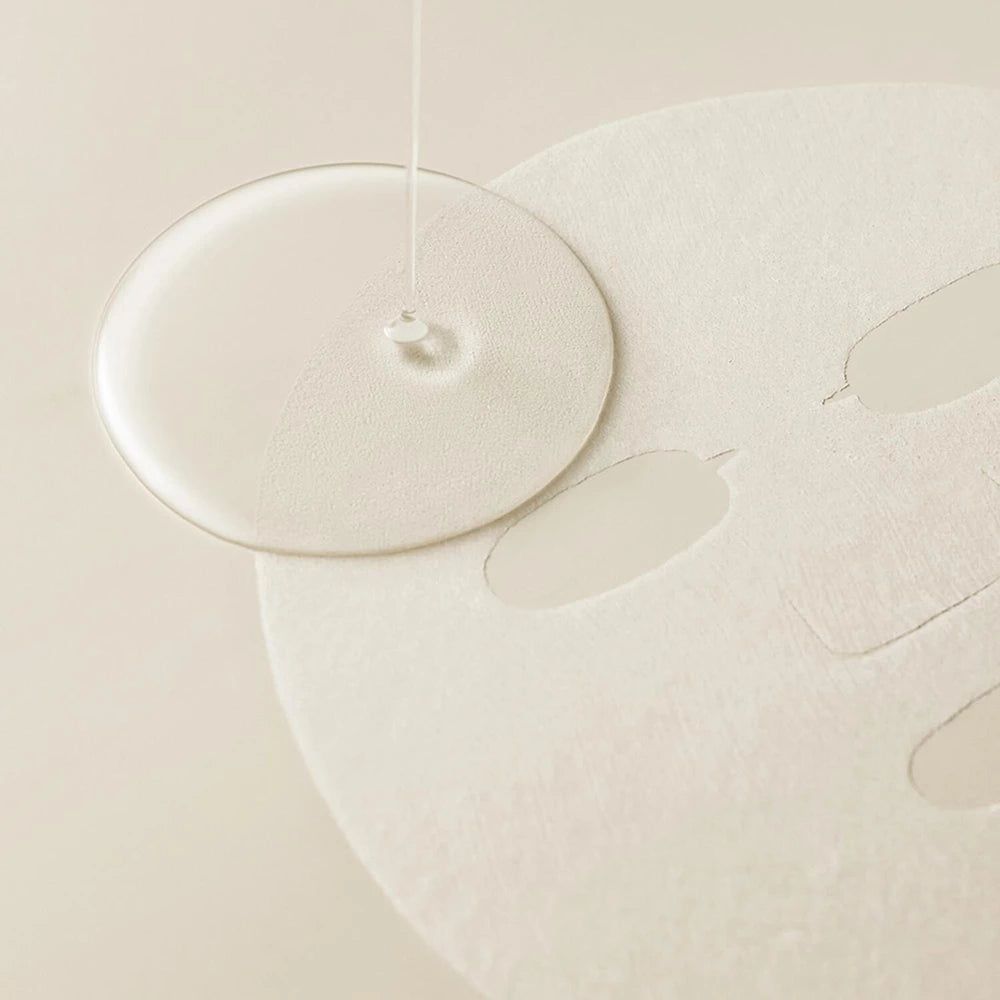 Klare Flüssigkeit tropft auf eine runde Maske. Die Maske hat Aussparungen für Augen, Nase und Mund.