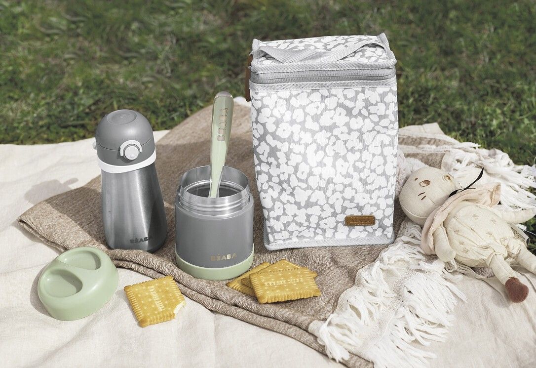 Thermo-Portionsbehälter, grau, hellgrün. Mit Zubehör: Tasche, Löffel, Deckel, Spielzeug. Auf Decke.