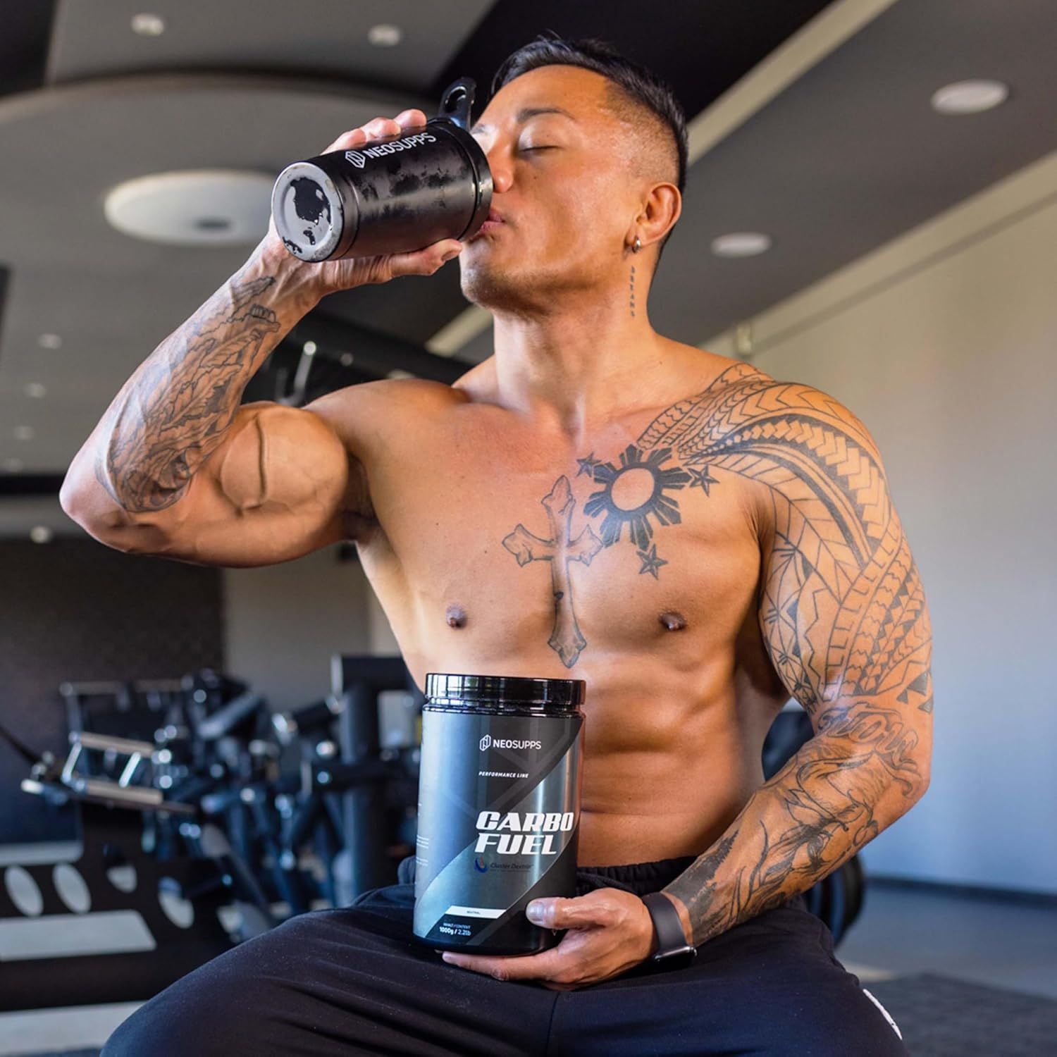 Mann trinkt aus schwarzer Trinkflasche. Hält Dose "CARBO FUEL". Tattoos.