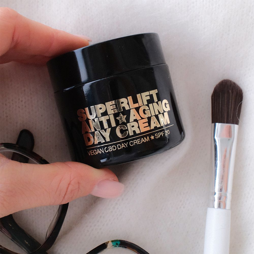 Schwarzer Tiegel mit goldfarbenem Text: Superlift Anti-Aging Day Cream. Daneben Pinsel und Brille.