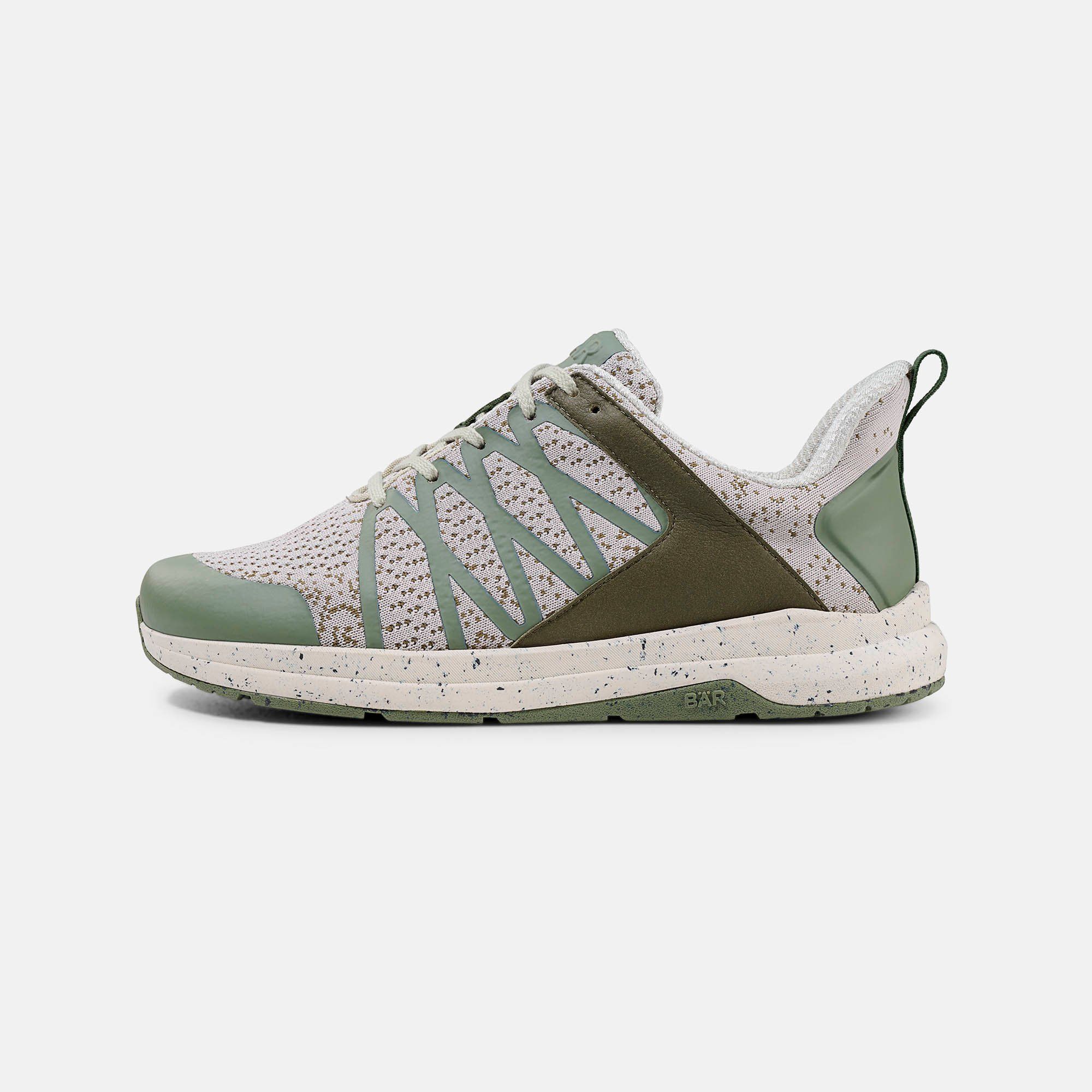 Ein grüner und beiger Schnürschuh. Mesh-Obermaterial, grüne Akzente, weiße Sohle mit Flecken. BÄR-Logo.