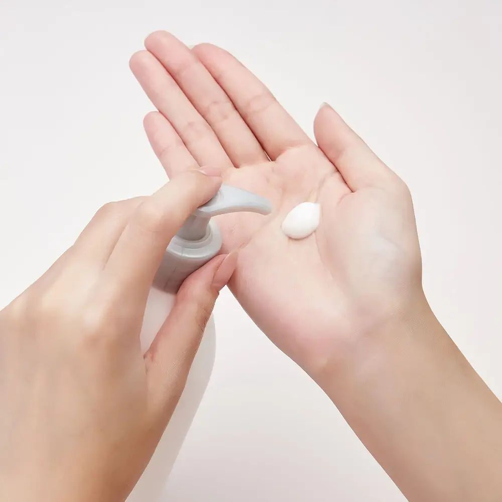 Hände halten eine weiße Creme. Eine kleine Menge Creme wird aus einer Pumpe in die Handfläche gespritzt.
