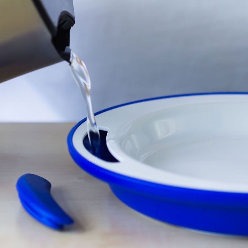 Blauer Teller mit weißem Innenraum. Wasser wird aus einem Wasserkocher in den Teller gegossen. Ein Griff liegt daneben.