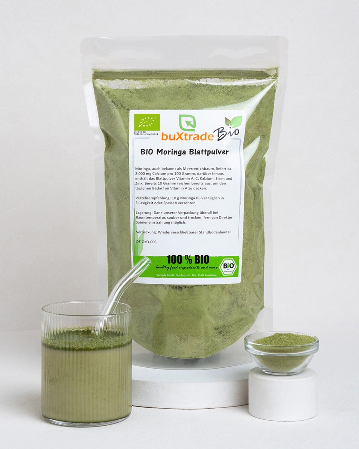 Bio Moringa Blattpulver in einem Beutel, daneben ein Glas mit Moringa-Getränk und eine Schale mit Pulver.