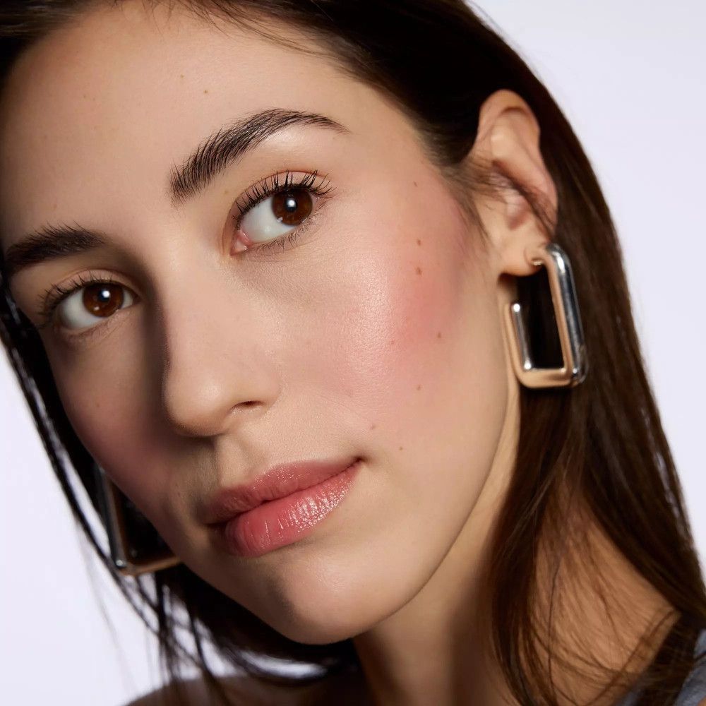 Porträt einer Frau mit Rouge auf den Wangen. Sie trägt Ohrringe. Helles Make-up.