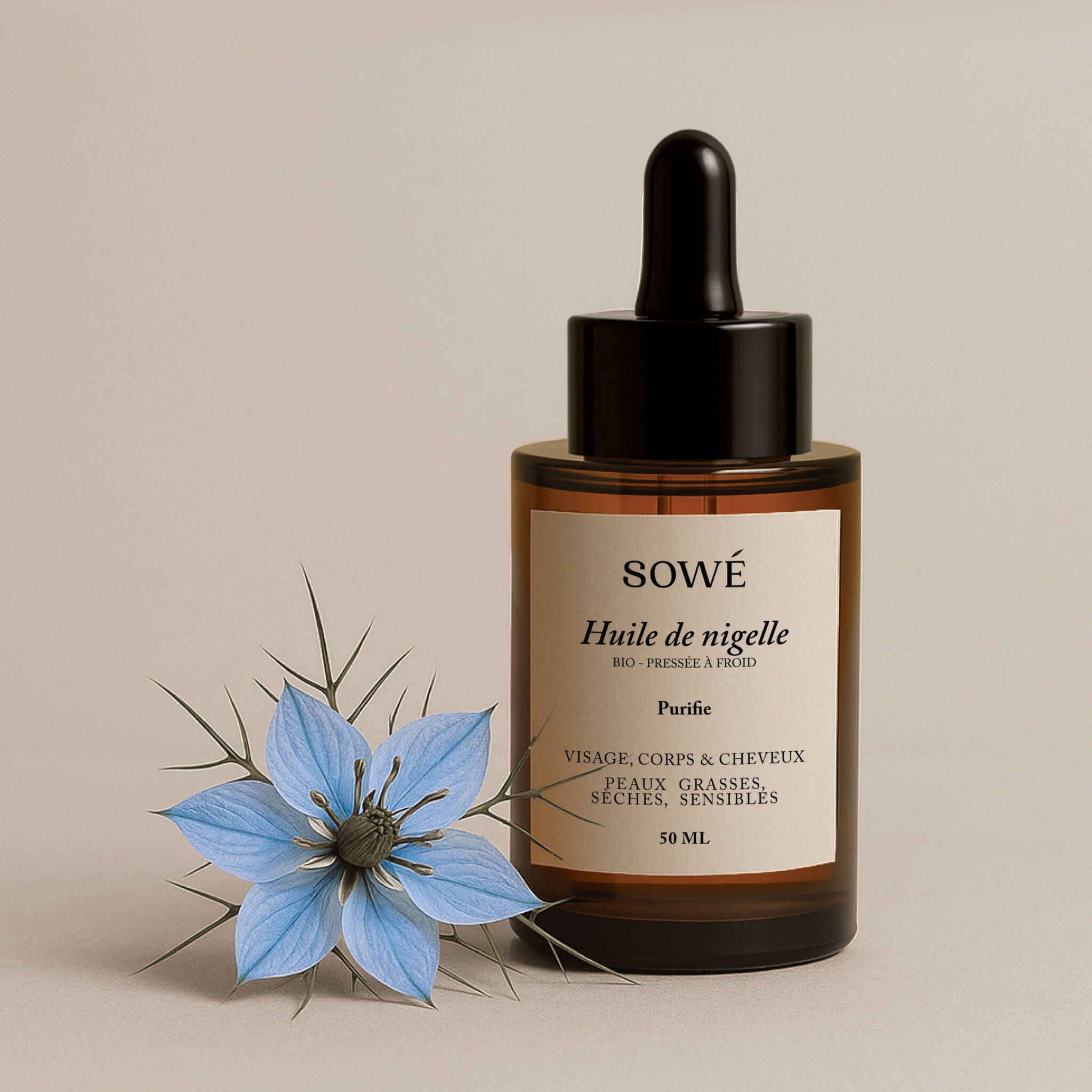 Braune Glasflasche mit Pipette. Etikett "SOWÉ Huile de nigelle". Blaue Blume daneben.