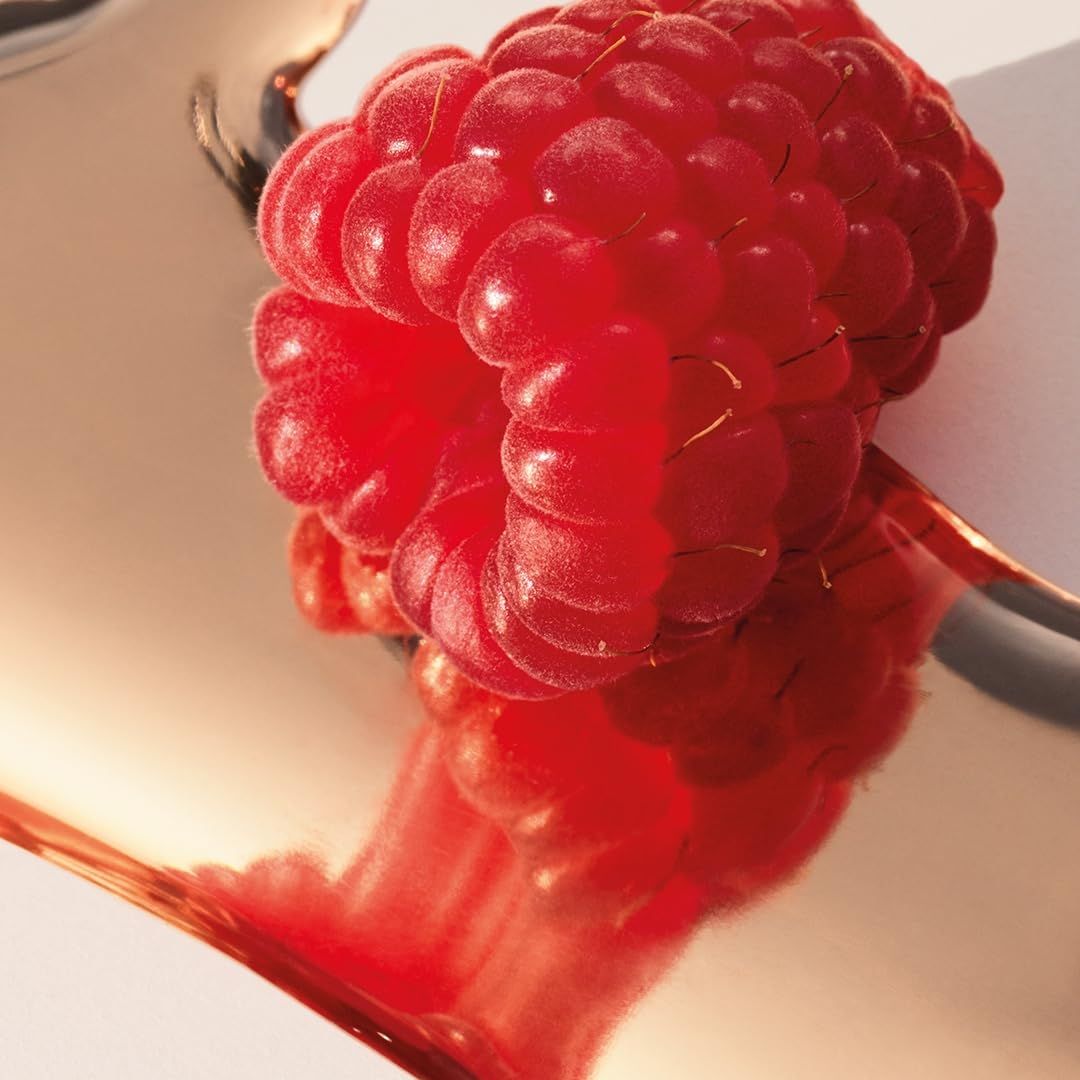 Eine rote Himbeere auf einer spiegelnden, kupferfarbenen Oberfläche.