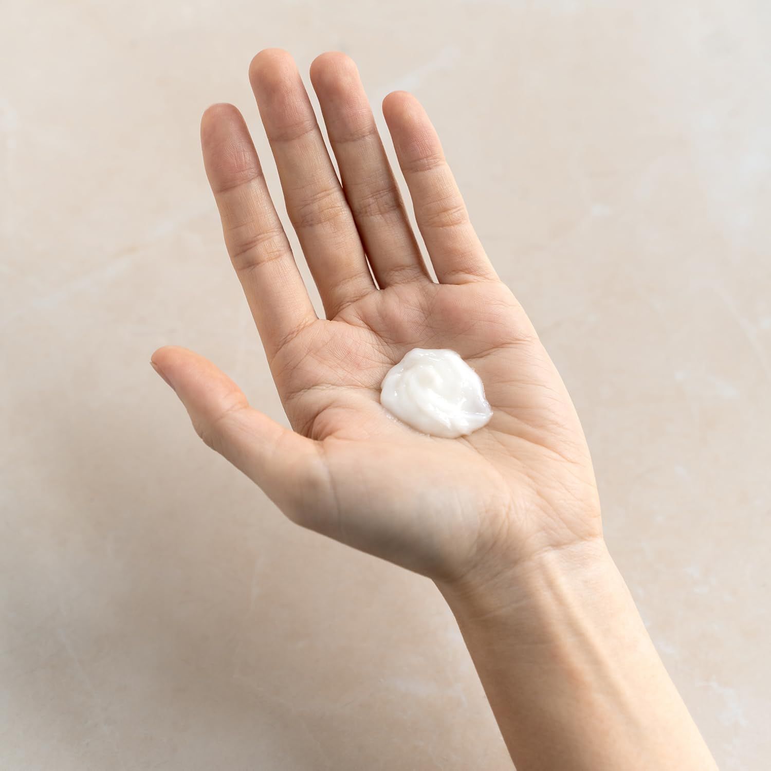Hand mit einer kleinen Menge weißer Creme. Helle Haut, glatter Hintergrund.