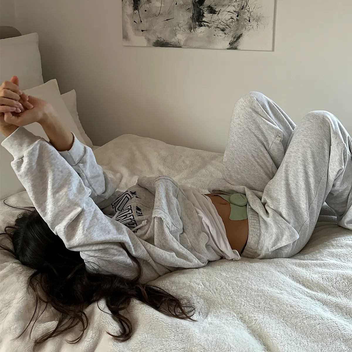 Frau in Jogginghose liegt auf einem Bett, ein grünes Flow-Pad ist auf ihrem Bauch sichtbar.